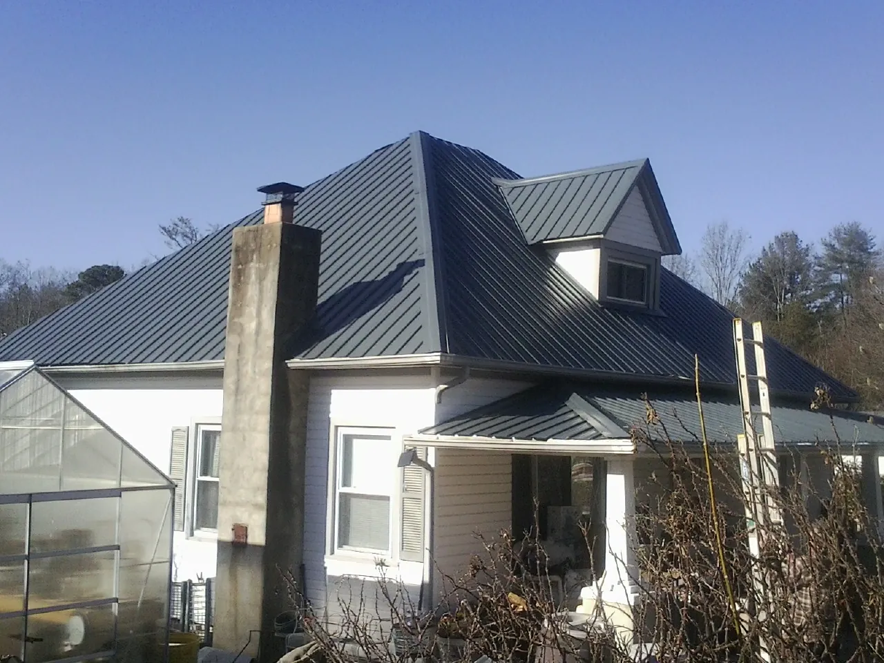 Dark blue standing seam metal roof on a white farmhouse with dormer — Slate & Tile Roof Repair by Roofing Brothers in Swanton