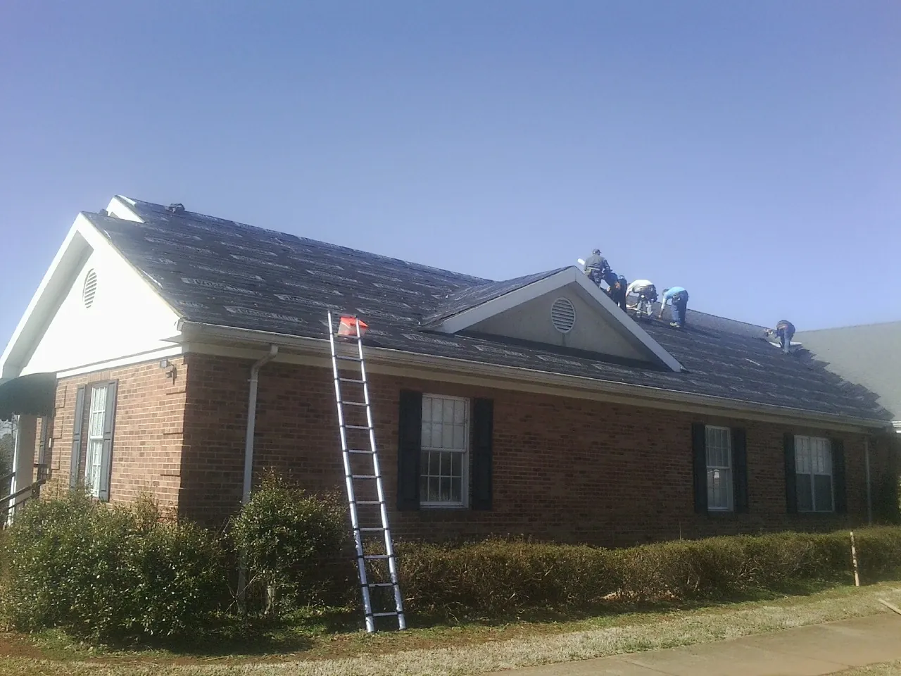 Crew tearing shingles off a brick ranch roof with a ladder set — Emergency Roof Repair work by our crew in Swanton