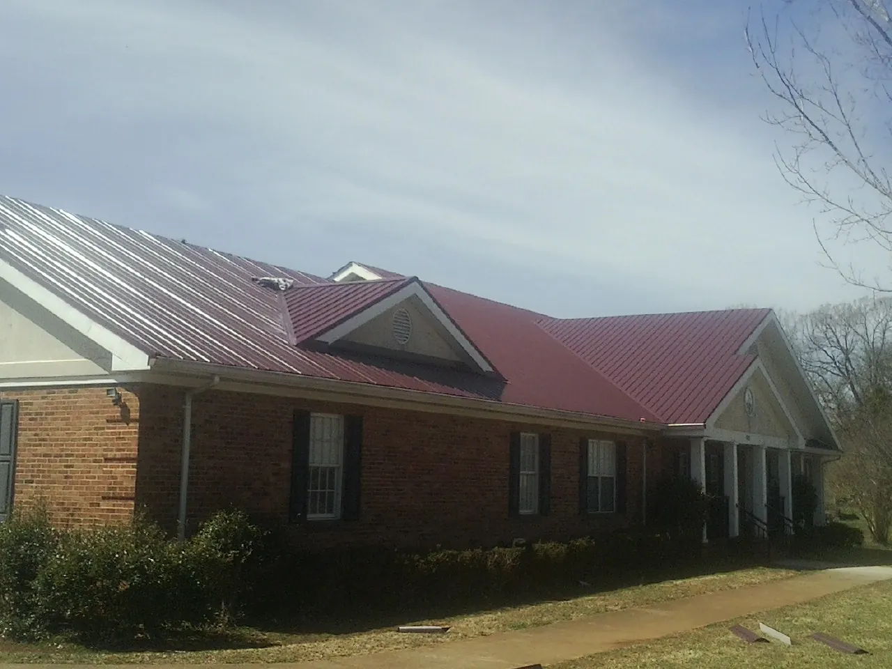 Red metal roof with gabled entries on a long brick building, from a Hail Damage Roof Repair job in Swanton