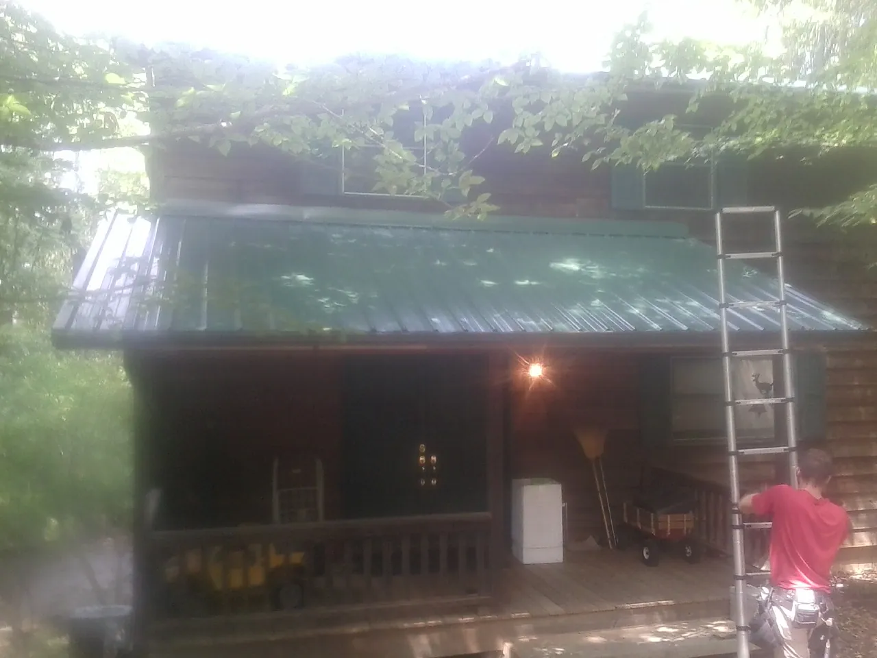 Worker on a ladder at the green porch roof of a wooded cabin in Swanton