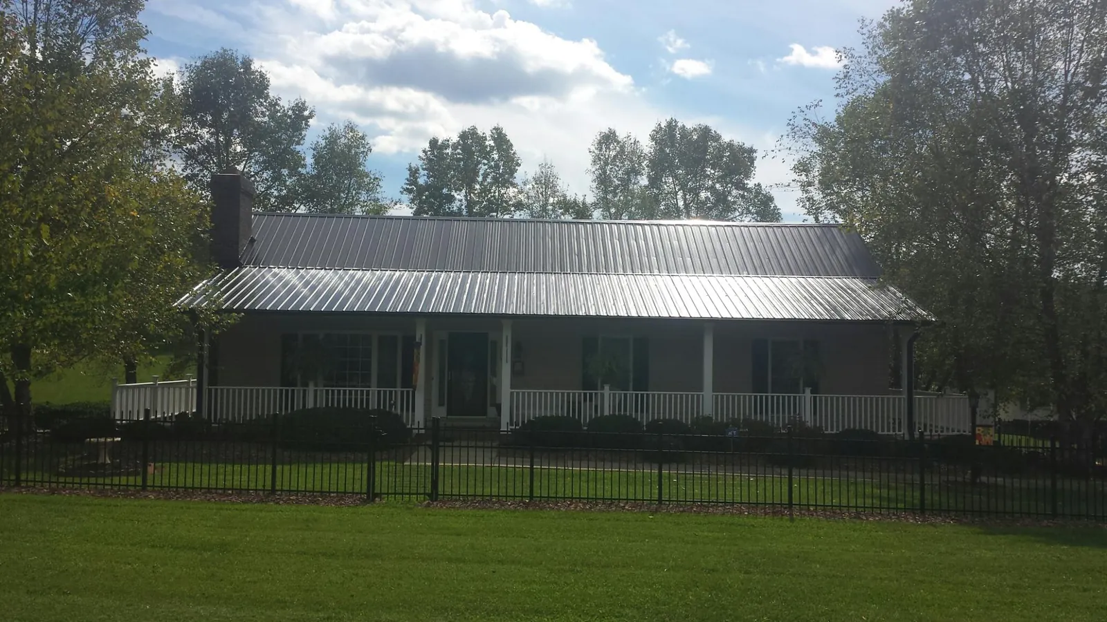 Gray metal roof on a brick ranch with a full width front porch — Gutter Guard Installation work by our crew in Swanton